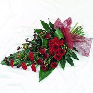 Deep red seasonal floral funeral spray with foliage, wrapped in luxury cellophane and a bow.