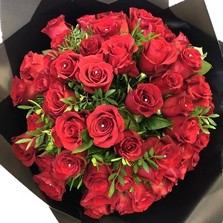 Luxury hand-tied bouquet of 50 large-headed red Freedom roses with sparkling diamanté centres and complementary foliage, wrapped in luxury cellophane and presented in a signature black gift bag with rope handles.