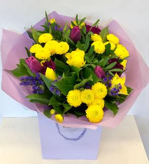 Spring bouquet including yellow roses and chrysanthemums and purple tulips and statice.