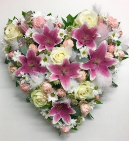 Mixed floral heart with lily, roses and chrysanthemum finished with white feathers, diamantes and glitter dusting. 