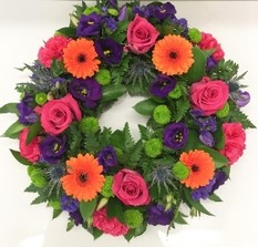 Vibrant funeral wreath with cerise, orange, purple, and lime green flowers on a rich green foliage base.