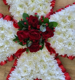 Maltese cross funeral tribute with massed white chrysanthemum and red focal and ribbon edge. 