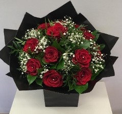 Twelve luxury red roses with white gypsophila, accented with complementary foliage, wrapped in luxury cellophane and matching gift bag, hand-tied in water.