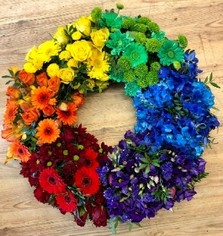 Vibrant funeral wreath with mixed seasonal flowers arranged in a rainbow pattern of red, orange, yellow, green, blue, and purple.