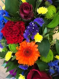 Elegant funeral wreath with vibrant flowers in orange, red, blue, purple, green, and yellow, accented with lush foliage.