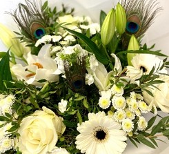 Elegant white bouquet featuring lilies, roses, alstroemeria, and chrysanthemums, accented with vibrant peacock feathers and presented in a luxury hatbox.