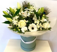 Elegant white bouquet featuring lilies, roses, alstroemeria, and chrysanthemums, accented with vibrant peacock feathers and presented in a luxury hatbox.
