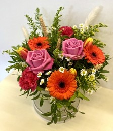 Arrangement design that includes vivid tones of roses, germini and daisy's finished with corn and pampas grass in a luxury hat box. 