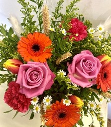 Arrangement design that includes vivid tones of roses, germini and daisy's finished with corn and pampas grass in a luxury hat box. 