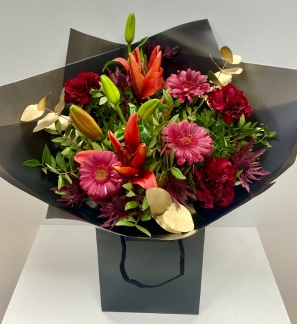 This beautiful bouquet is filled with warm reds and burgundy tones and finished with a pop of gold leaf eucalyptus. Wrapped in our classic black cellophane and signature gift bag in water. 
