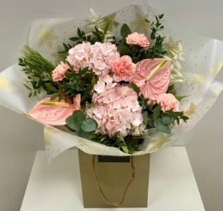 Soft pink hydrangea and peach carnation paired with a show stopping glimmering pink anthurium and mixed foliage. This design is presented in our festive cellophane and signature gift bag in water. 