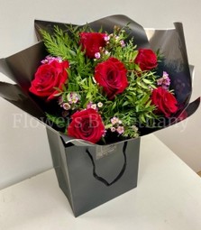 Bouquet featuring 6 luxury red roses with pink wax flowers, accented with diamanté in the roses, complemented by foliage, wrapped in luxury cellophane and matching gift bag, hand-tied in water.