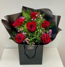 Bouquet featuring 6 luxury red roses with pink wax flowers, accented with diamanté in the roses, complemented by foliage, wrapped in luxury cellophane and matching gift bag, hand-tied in water.