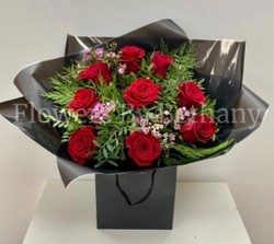 Bouquet of nine luxury red Freedom roses with pink wax flowers, accented with diamanté and complementary foliage, wrapped in luxury cellophane and matching gift bag, hand-tied in water.