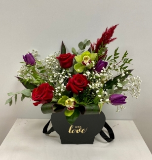 New heart shaped black carrier, design includes red roses, purple tulips, green orchids and finished with mixed foliage and pampas grass. 