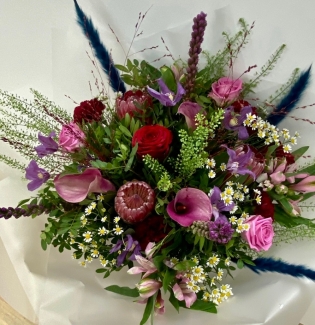 Hand tied bouquet boasting ruby red's, tanzanite and amethyst tones including roses, calla lily and clematis. 