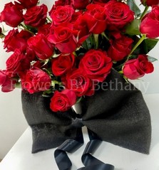 Heart-shaped arrangement of 50 red roses in a matte black hatbox, finished with a large bow.
