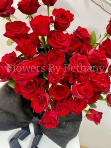 Heart-shaped arrangement of 50 red roses in a matte black hatbox, finished with a large bow.