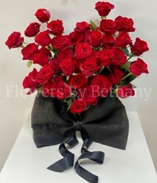 Heart-shaped arrangement of 50 red roses in a matte black hatbox, finished with a large bow.