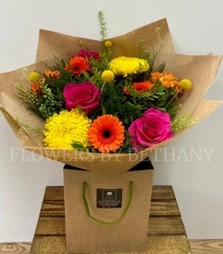 A bright bouquet in orange, yellow and cerise. Including roses, germini, spray rose, green bell and more. Presented in a kraft bag and wrap. 