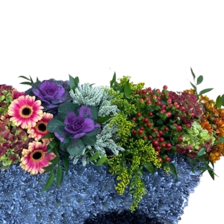 Wheelbarrow funeral tribute, with overflowing florals in mixed vibrant tones. 