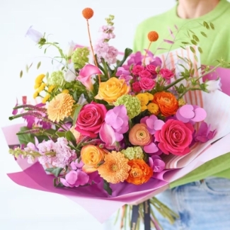 Bright colourful hand-tied bouquet with mixed seasonal florist’s choice florals in pink, yellow, orange and purple tones.