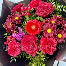 Sparkling bouquet featuring luxury red Freedom roses, red carnations, and red hypericum berries, accented with diamante centers, red glitter, and a pink butterfly, wrapped in luxury cellophane and matching gift bag, hand-tied in water.