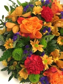 Sunset-themed funeral wreath with orange, red, and purple flowers, accented with green filler florals on a lush foliage base.