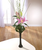 Single pink lily comes presented with leaves and grass in a glass vase. 