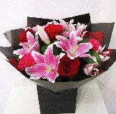 Bouquet featuring luxury red Freedom roses, cerise carnations, and pink lilies, accented with complementary foliage, wrapped in luxury cellophane and matching gift bag, hand-tied in water.