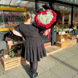 Valentine’s bouquet made with 24 premium red roses arranged around a white gypsophila heart with a pearl bow, wrapped in black with red ribbon, designed out of water with options for a gift bag with water bubble or upgrade to a modern glass vase.