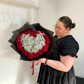 Valentine’s bouquet made with 24 premium red roses arranged around a white gypsophila heart with a pearl bow, wrapped in black with red ribbon, designed out of water with options for a gift bag with water bubble or upgrade to a modern glass vase.