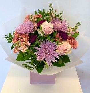 Hand tied bouquet of blooms, carnations, roses, chrysanthemums and stocks in warm autumn tones. 