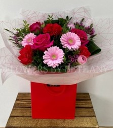 Stunning bouquet filled with bright pink and bold red tones including roses, carnations and germini presented in our signature gift bag in water. 