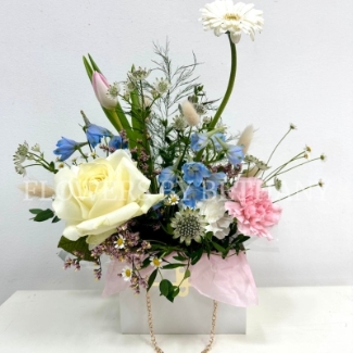 A beautiful gift bag with mixed pastel spring florals including tulips, delphinium, rose and matricaria. 