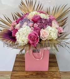 Elegant bouquet with roses, spray roses, and hydrangea, accented with gold leaf and an ombré palm, presented in a signature gift bag.