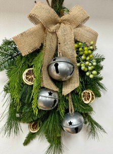 Natural door swag filled with winter foliage, green berries, lime slices, silver bells and a hessian bow. 