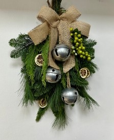 Natural door swag filled with winter foliage, green berries, lime slices, silver bells and a hessian bow. 