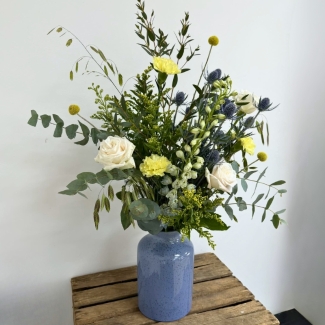 Highland Meadow vase arrangement featuring seasonal ivory, yellow and blue-toned florals with natural meadow-style movement, arranged in a blue ceramic vase by Flowers by Bethany.