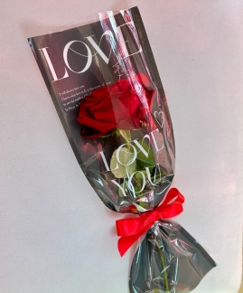 A single red rose elegantly cradled in a paper wrap adorned with heartfelt words of love.