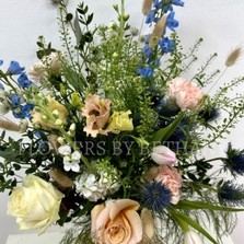 A hand tied bouquet filled with seasonal varities in peach, pink and blue tones presented in a glass vase with a bow. 