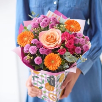 Petite hand-tied bouquet with mixed seasonal florist’s choice florals in peach, pink and orange tones, presented in a patterned gift box.