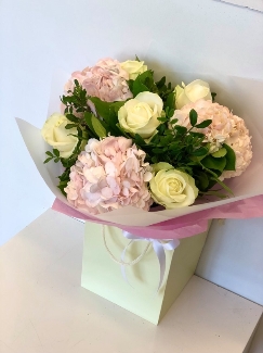 Hand tied bouquet of soft pink hydrangea and white roses, wrapped in luxury cellophane and a gift bag. 