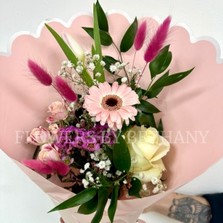 A petite hand tied bouquet in mixed pink hues in a pink scalloped wrap with positivity script. 