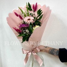 A petite hand tied bouquet in mixed pink hues in a pink scalloped wrap with positivity script. 