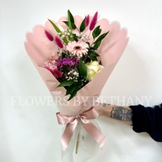 A petite hand tied bouquet in mixed pink hues in a pink scalloped wrap with positivity script. 