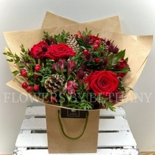 Mixed red bouquet including roses, alstroemeria, hypericum and thistle. Wrapped in kraft paper and displayed in a kraft bag. 