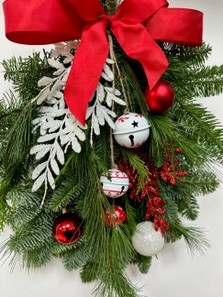Red and white door swag, a bundle of winter foliage decorated with baubles, glitter foliage, bells and a red bow. 