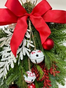 Red and white door swag, a bundle of winter foliage decorated with baubles, glitter foliage, bells and a red bow. 