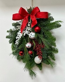 Red and white door swag, a bundle of winter foliage decorated with baubles, glitter foliage, bells and a red bow. 